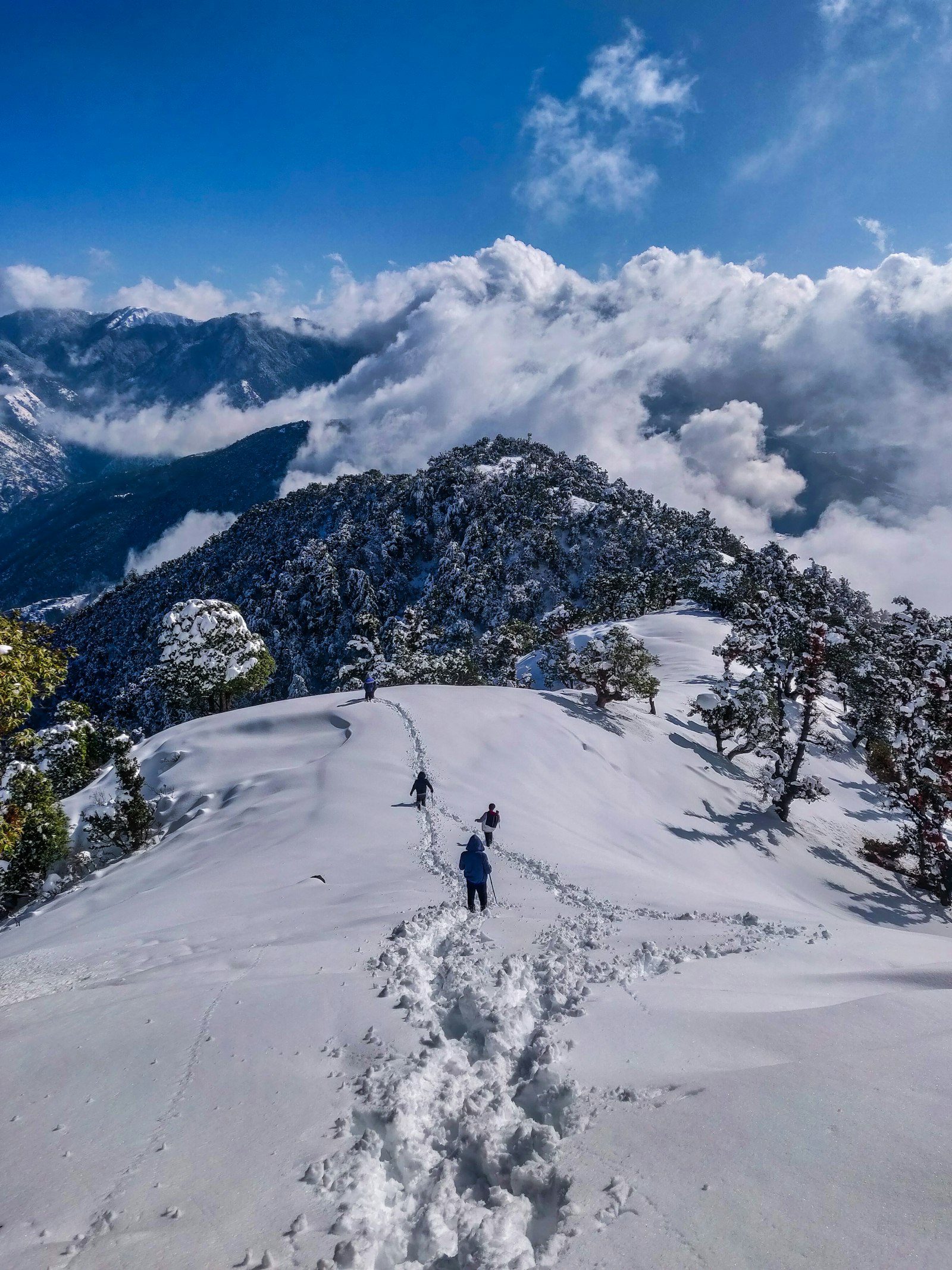 Travellers walking a snowy Himalayan ridge above the clouds in Himachal Pradesh